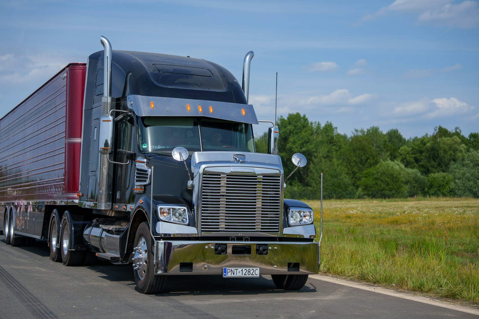 Black semi truck with a refrigerated trailer on a country road